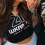 A man and a woman posing together outdoors. The man is wearing a black graphic t-shirt with a horror movie poster design, a gray baseball cap backwards, and sunglasses.